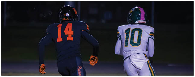 Two people in football uniforms with numbers 14 and 10 are running on a field at night. Description generated by AI