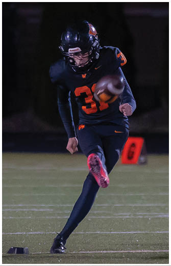 A person wearing a black football uniform with the number 39 is kicking a football on a field at night. Description generated by AI