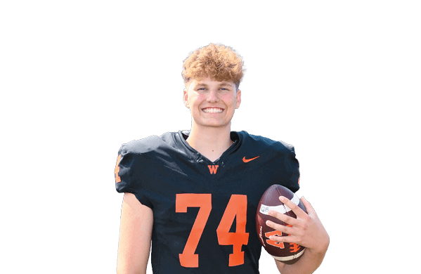 A person with curly hair wearing a black football jersey with the number 74 is smiling and holding a football. Description generated by AI