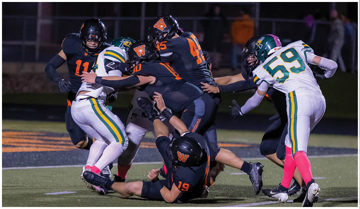 A group of people wearing football uniforms are engaged in a tackle on a field during a game. Description generated by AI