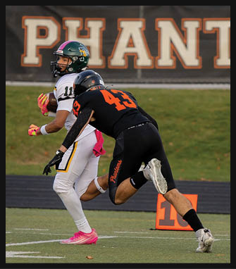 Three people in black and orange football uniforms are running on a field near an orange yard marker with a blurred background showing part of a sign. Description generated by AI