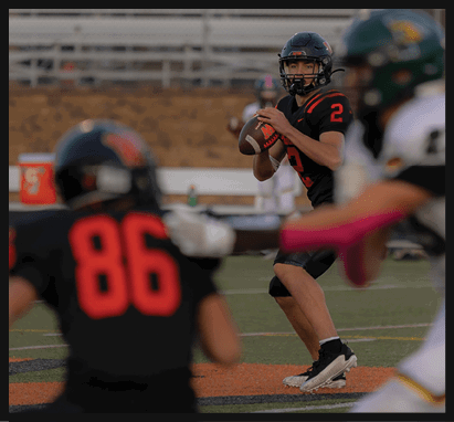 Two people in black and red football uniforms are on a field with one preparing to throw a football and the other facing them. Description generated by AI