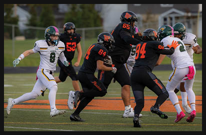 Adults in football uniforms are actively engaged in a game on a field, with some players running and others blocking or tackling. Description generated by AI