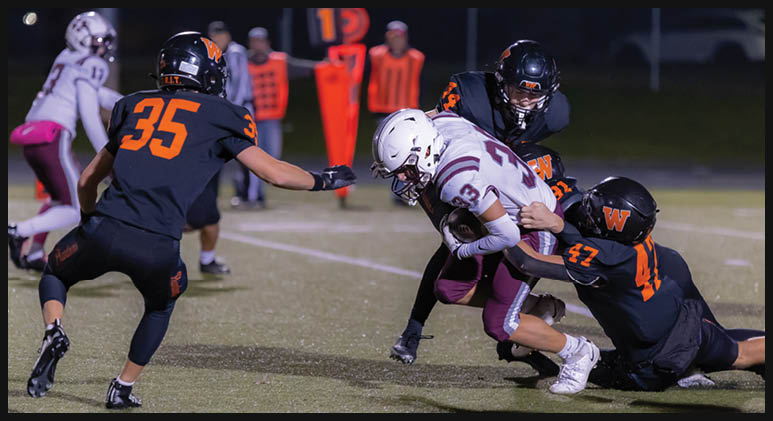 A group of people in football uniforms are actively engaged in a tackle on a grassy field during a game. Description generated by AI