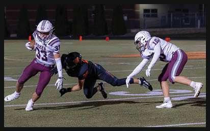 Three people in football uniforms are on a field with one person in black diving toward two people in white and maroon uniforms who are moving to catch or block them. Description generated by AI
