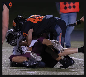 Two people in football gear are engaged in a tackle on a field during a game at night. Description generated by AI