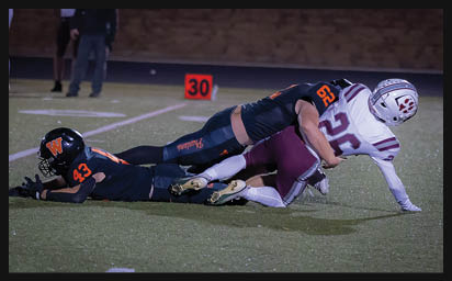 Two people in football uniforms are on the ground during a tackle on a football field near a yard marker. Description generated by AI