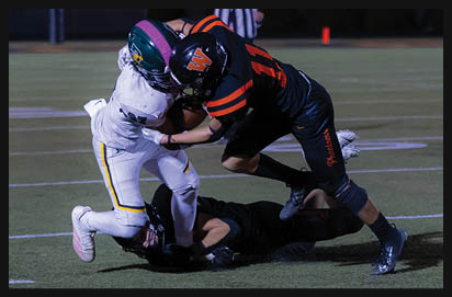 Two people in football uniforms are tackling a third person who is lying on the ground during a game on a grassy field. Description generated by AI