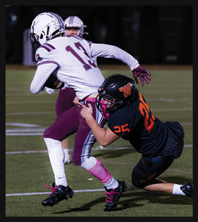 Two people in football uniforms are engaged in a tackle on a grassy field during a game. Description generated by AI