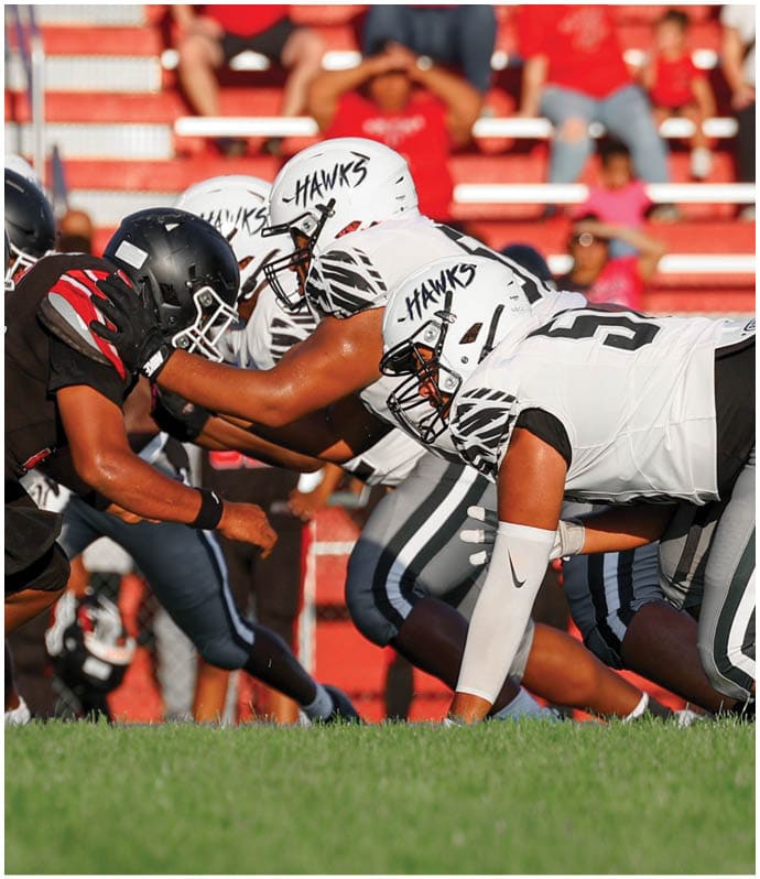 Two opposing American football teams in black and white uniforms are lined up facing each other on a grassy field, ready for the next play. Descripci n generada con IA