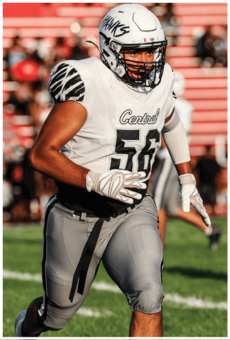 An adult wearing a white football jersey with the number 56 and the word Central is running on a field while wearing a helmet and gloves. Descripci n generada con IA