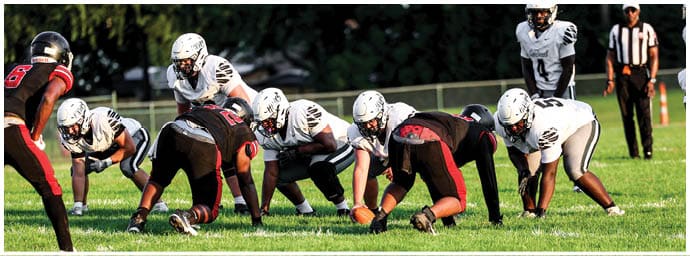 People in athletic clothing are positioned on a grassy field in a stance typical of a football game just before the play begins. Descripci n generada con IA