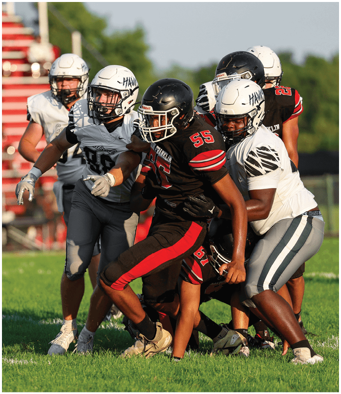 Several people wearing football uniforms are engaged in a close physical play on a grassy field. Descripci n generada con IA