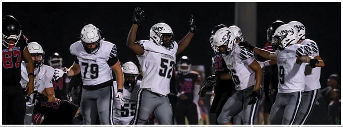 A group of people wearing football uniforms are gathered on a field at night, with one person raising their arms. Descripci n generada con IA