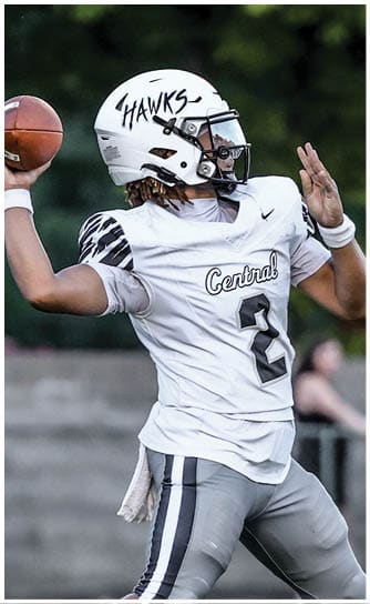 A person wearing a white football uniform with the word “Central" and the number 2 is preparing to throw a football on a grassy field. Descripci n generada con IA