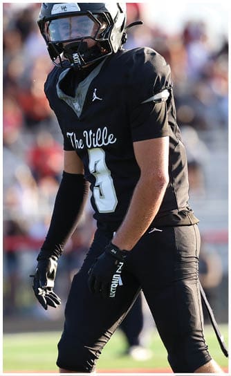 A person wearing a black football uniform with the number 8 and the words “The Ville" stands on a football field. Descripci n generada con IA