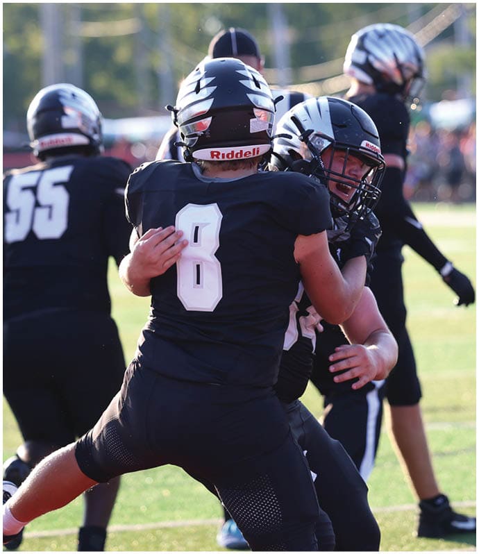 People wearing black football uniforms and helmets are engaged in a practice or game on a grassy field. Descripci n generada con IA