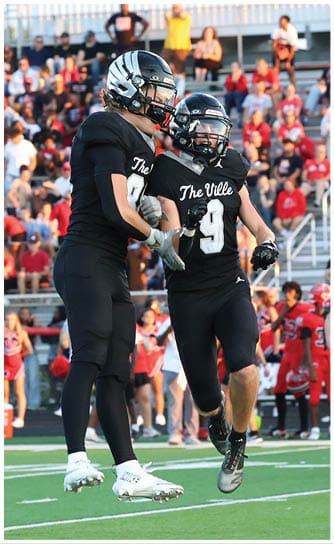 Three people in black football uniforms are on a field with one jumping in the air while a crowd watches from the stands in the background. Descripci n generada con IA