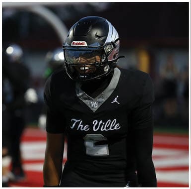Person wearing a black football helmet with a reflective visor and a black sports jersey with a logo on the shoulder. Descripci n generada con IA