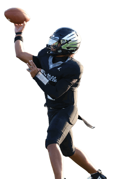 A person in black sports gear is throwing a football while another person in black gear is on the ground and a person in red sports gear is approaching on a football field with spectators in the background. Descripci n generada con IA