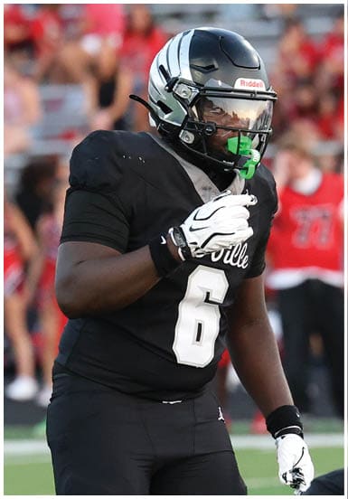 Two people in black football uniforms and helmets are positioned on a football field with a crowd in the background. Descripci n generada con IA