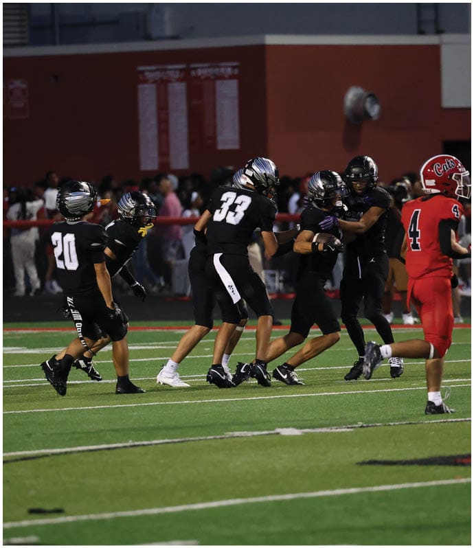 Several people in black sports uniforms are playing football on a field while one person in a red uniform stands nearby. Descripci n generada con IA
