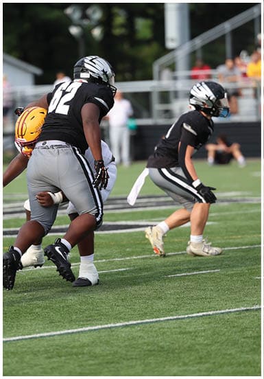 Two people in black and white football uniforms are positioned on a green field, appearing ready to engage in a play during a game. Descripci n generada con IA
