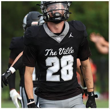 A person wearing a black football uniform with the number 28 and the words The Ville is on a field with another player in the background. Descripci n generada con IA