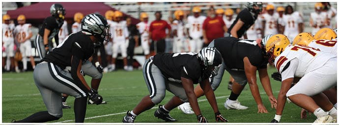People in football uniforms are crouched on a grassy field preparing for a play. Descripci n generada con IA