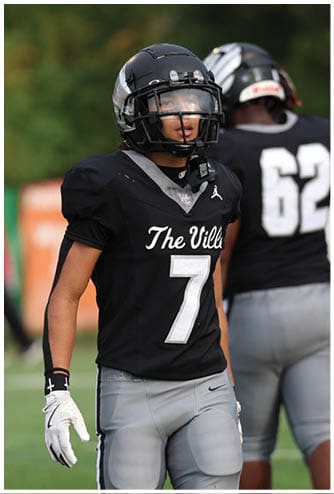 Three people wearing black football uniforms with helmets stand on a grassy field, with one facing forward and two facing away. Descripci n generada con IA
