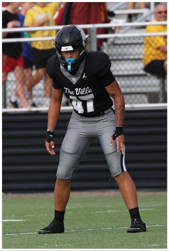 A person wearing a black football uniform with the number 43 is on a field with spectators and a scoreboard in the background. Descripci n generada con IA