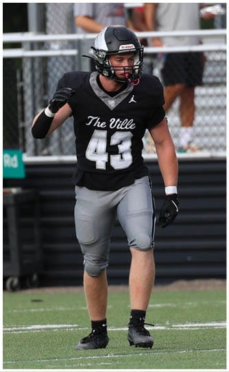 A person wearing a black football uniform with the number 43 is standing on a green football field with spectators in the background. Descripci n generada con IA