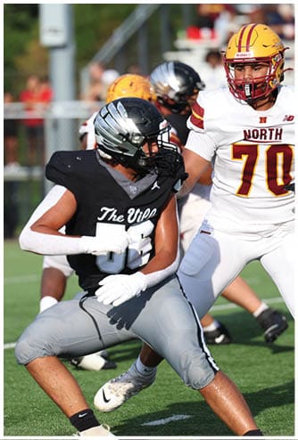 Two people wearing football uniforms and helmets are engaged in a play on a football field during a game. Descripci n generada con IA
