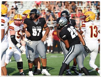 Several people wearing football helmets and uniforms are on a field with bleachers and spectators in the background. Descripci n generada con IA