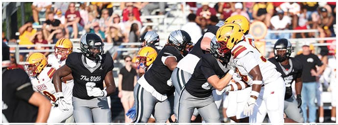 People in football uniforms are engaged in a play on a field with a crowd of spectators in the background. Descripci n generada con IA