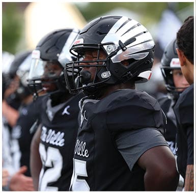 Two people wearing football helmets and uniforms are shown in close-up, facing sideways. Descripci n generada con IA