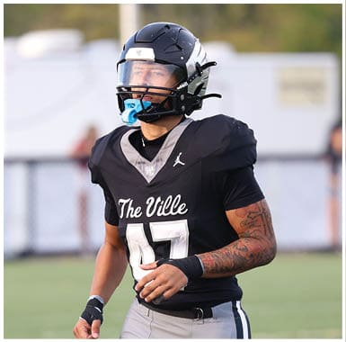 A person wearing a black football jersey with “The Ville" and the number 47 on it is standing on a field with a helmet and mouthguard. Descripci n generada con IA