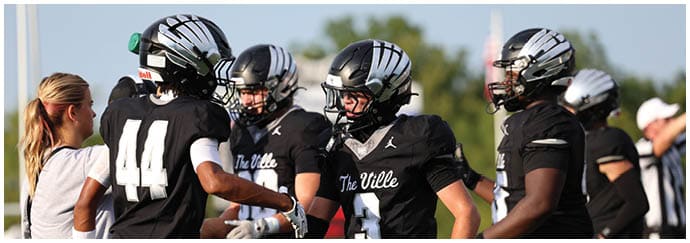People wearing black football uniforms with “The Ville" on the jerseys are interacting on a field. Descripci n generada con IA