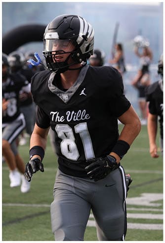 Several people wearing black football uniforms with “The Ville" on the front are running on a football field during a game or practice. Descripci n generada con IA
