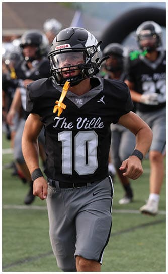 A person wearing a black football uniform with the number 10 and the words “The Ville" is running on a football field with other players in the background. Descripci n generada con IA