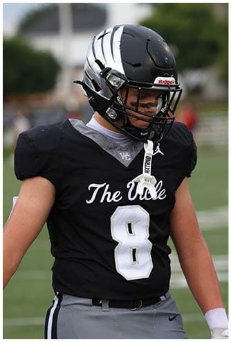 A person wearing a black football helmet and black jersey with the number 8 and the words The Vole stands on a football field. Descripci n generada con IA