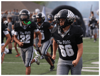A person wearing a black football uniform with the number 66 is running on a field with other players and cheerleaders in the background. Descripci n generada con IA