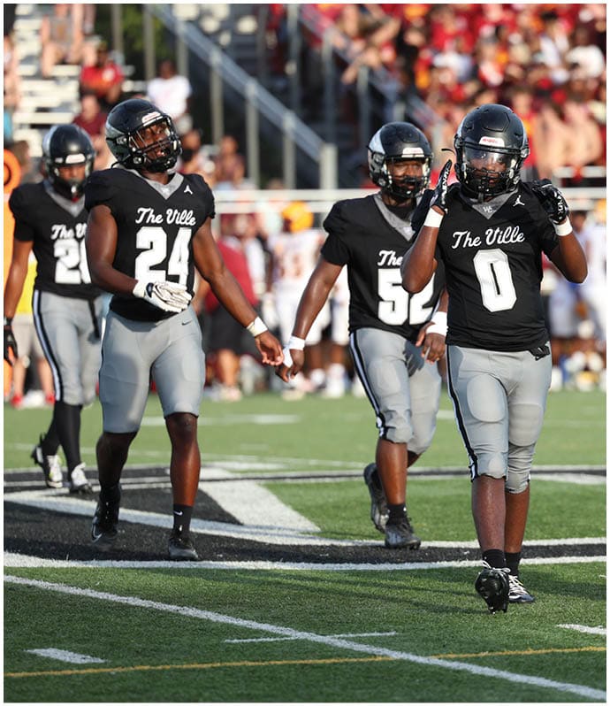 Several people in black sports uniforms are playing football on a field while one person in a red uniform stands nearby. Descripci n generada con IA