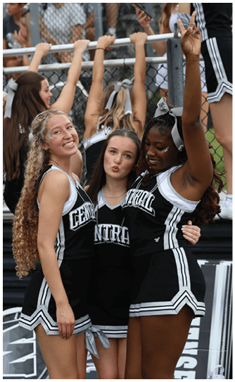 A group of people in black and white cheerleading uniforms are standing close together with one person raising their arms in celebration. Descripci n generada con IA