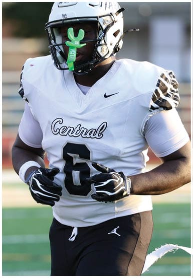 A person wearing a white football jersey with the word Central and the number 6 is on a football field, wearing black gloves and a helmet with a green mouthguard attached. Descripci n generada con IA