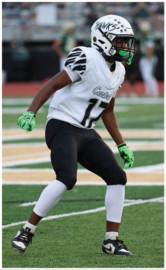 A person wearing a white football helmet and jersey with the number 17 is standing on a football field in a ready position. Descripci n generada con IA