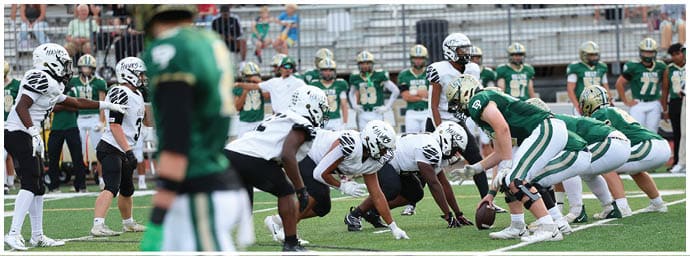 Two opposing American football teams in green and white uniforms are lined up facing each other on a field, preparing for a play. Descripci n generada con IA