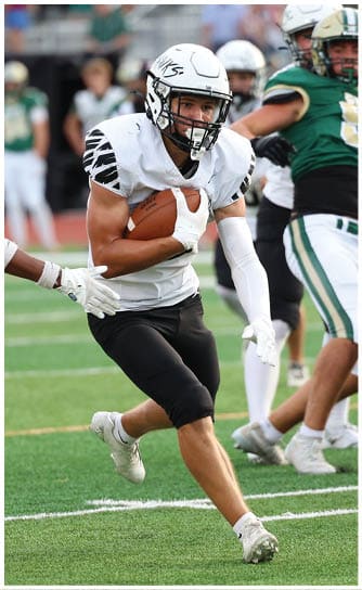 A person in a white football uniform is running with the ball while being pursued by players in green and white uniforms on a football field. Descripci n generada con IA
