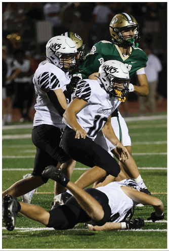 Two people in football uniforms are on a field with one person lying on the ground and the other running or moving forward. Descripci n generada con IA