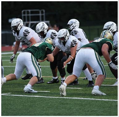 People in football uniforms from two teams are lined up on a field preparing for a play during a game. Descripci n generada con IA